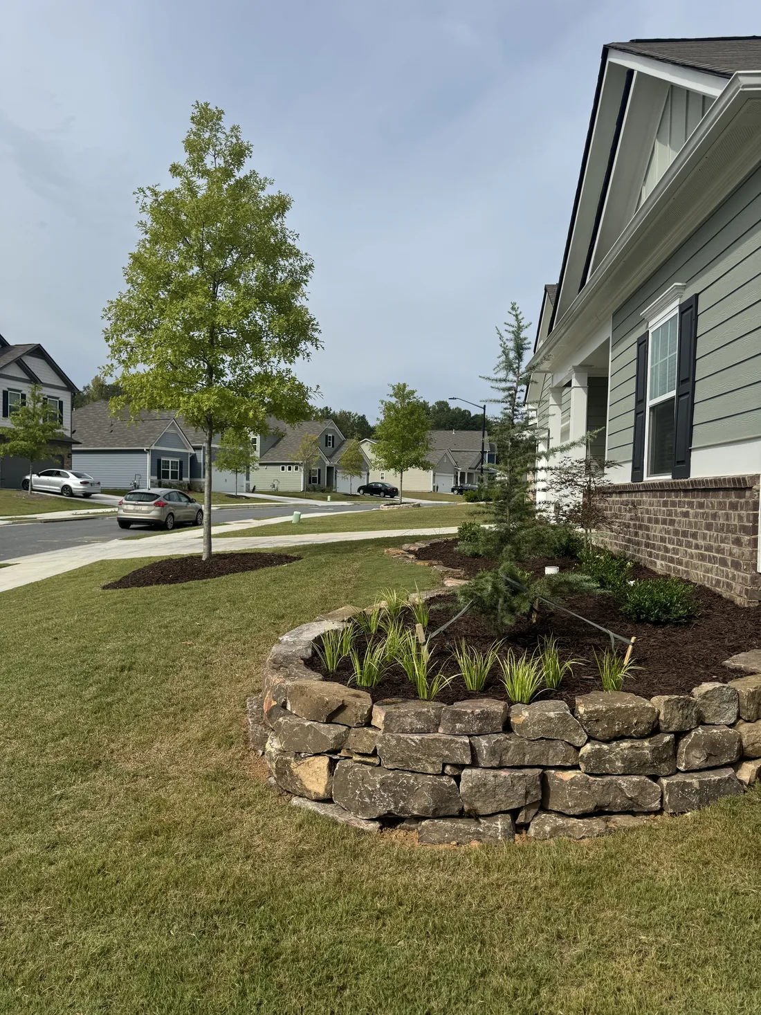 Curbside stacked-stone raised bed with ornamental grasses and a healthy lawn at an Acworth, Georgia home landscaped by KalKare