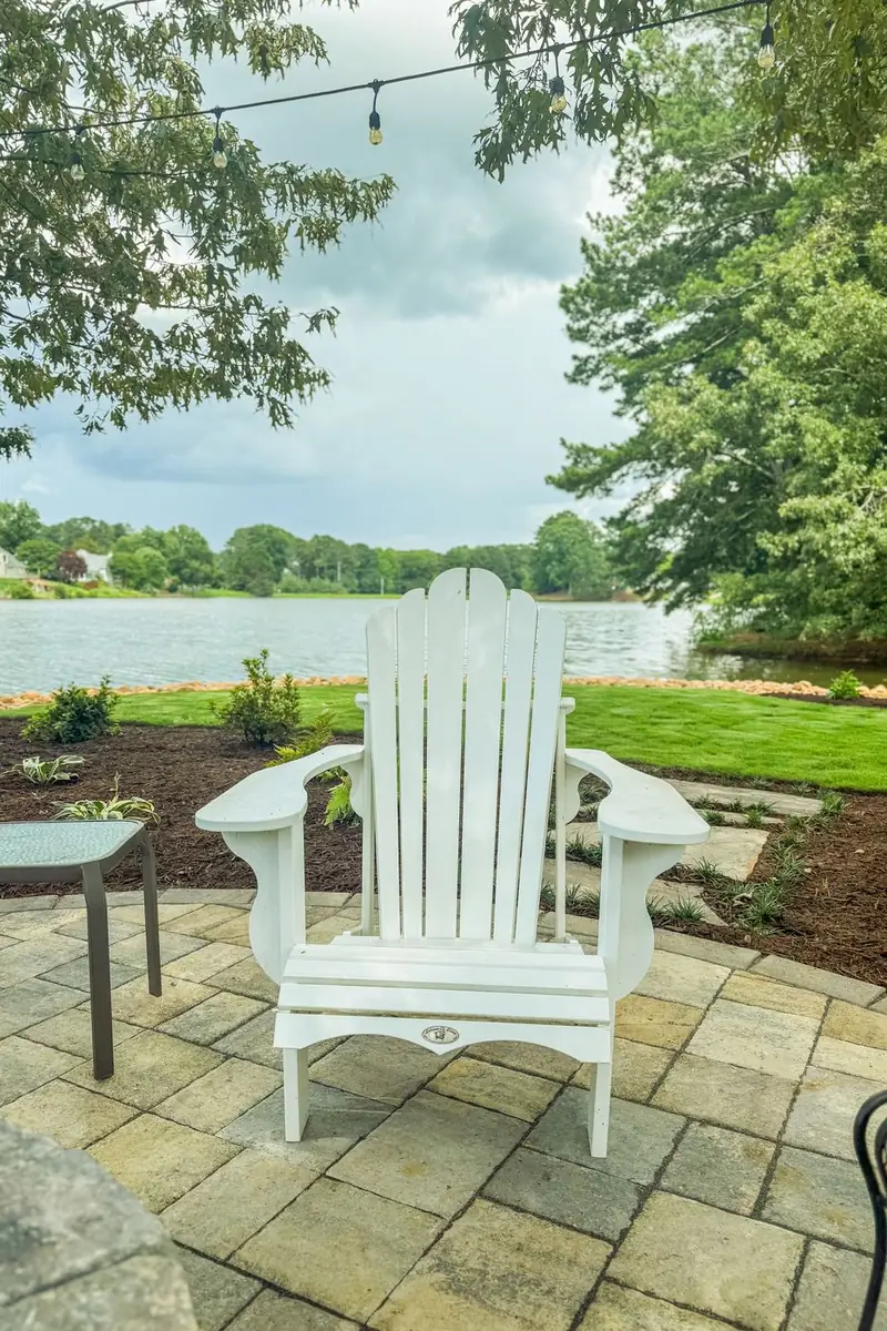 White adirondack chairs on a paver patio overlooking the lake.