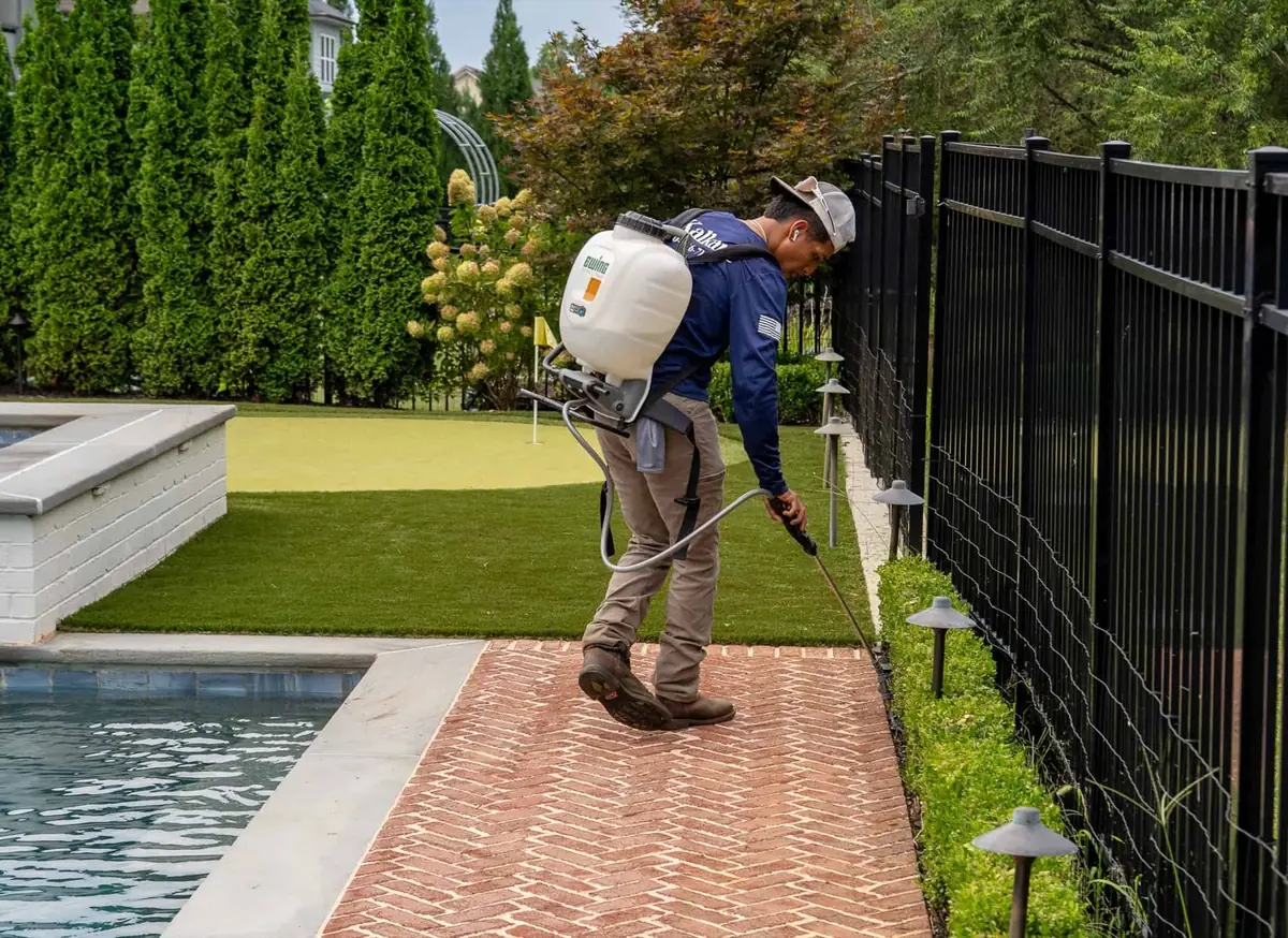 KalKare technician applying treatment along an iron fence beside a pool and brick walkway