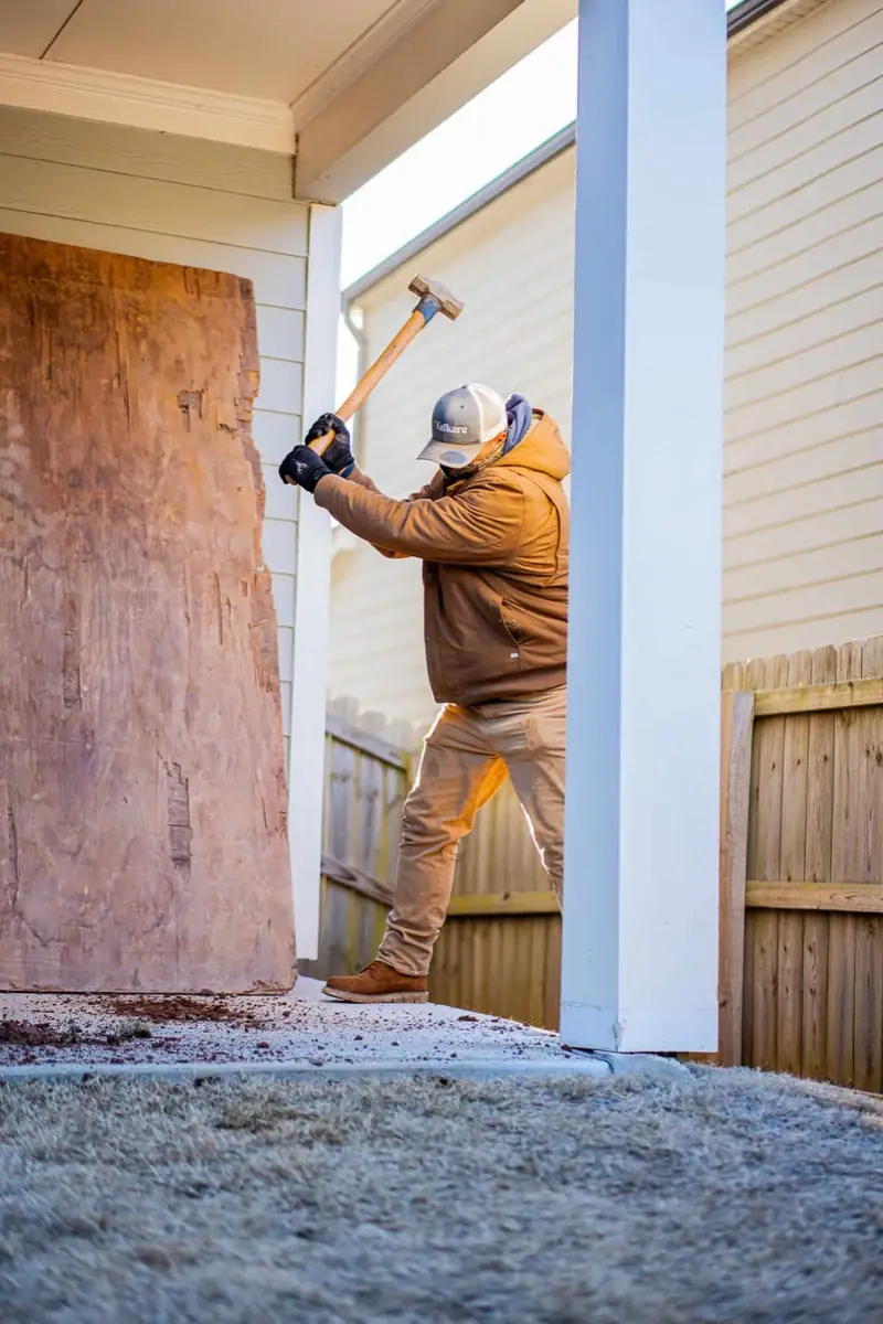 KalKare crew member swinging a sledgehammer during demolition beside a porch column