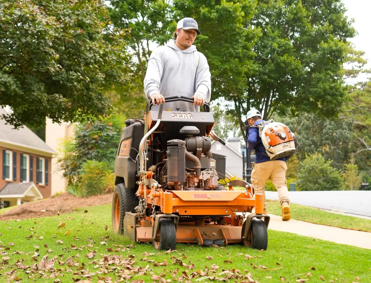 Two KalKare crew members maintaining a lawn, one on a stand-on mower and one with a backpack blower