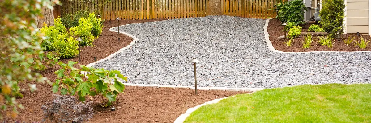 Finished KalKare project: a curved gravel pathway with stone edging, path lighting, and fresh mulched beds
