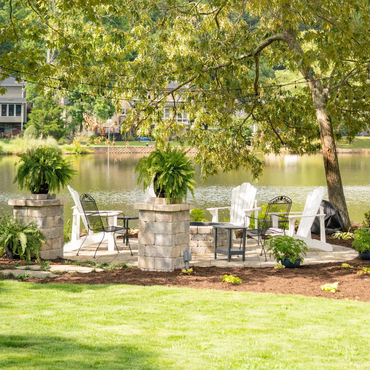 Lakeside stone patio with seating, stacked stone columns and ferns overlooking the water