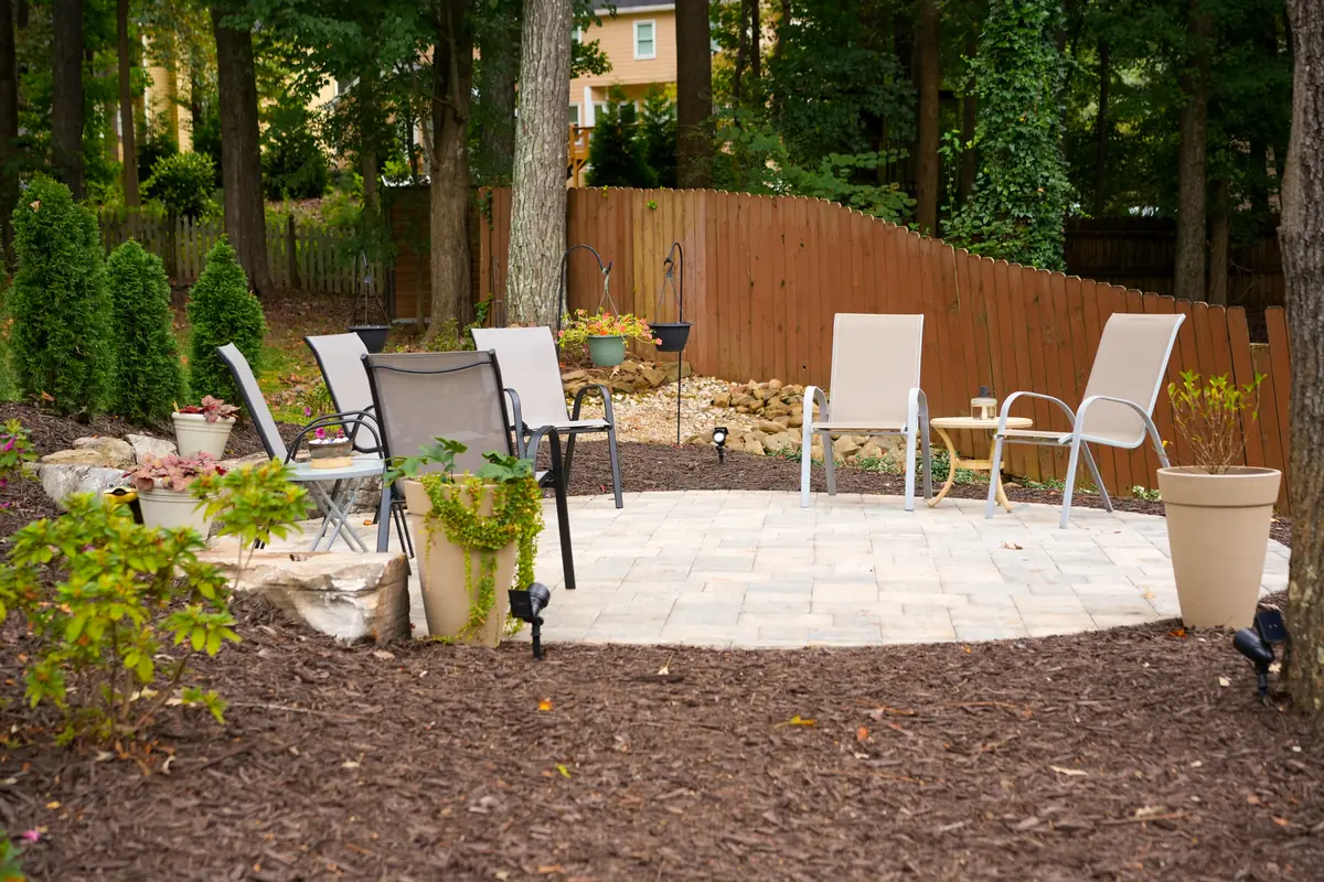 Finished paver patio with seating in a wooded backyard behind a privacy fence