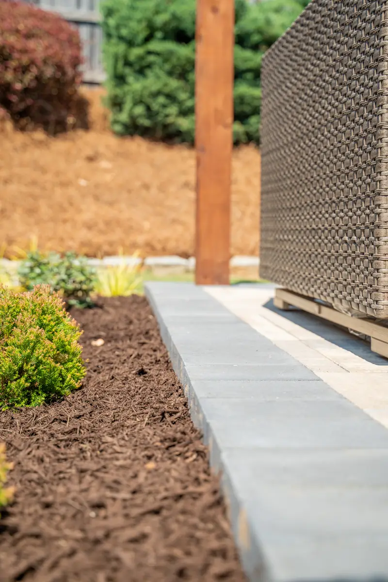 Close-up of a paver patio edge with a charcoal stone border against a mulched planting bed