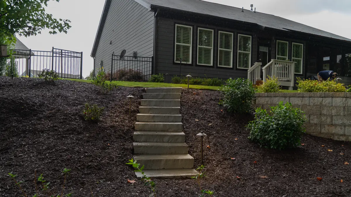 Stone steps set into a mulched slope with landscape lighting leading up to a home