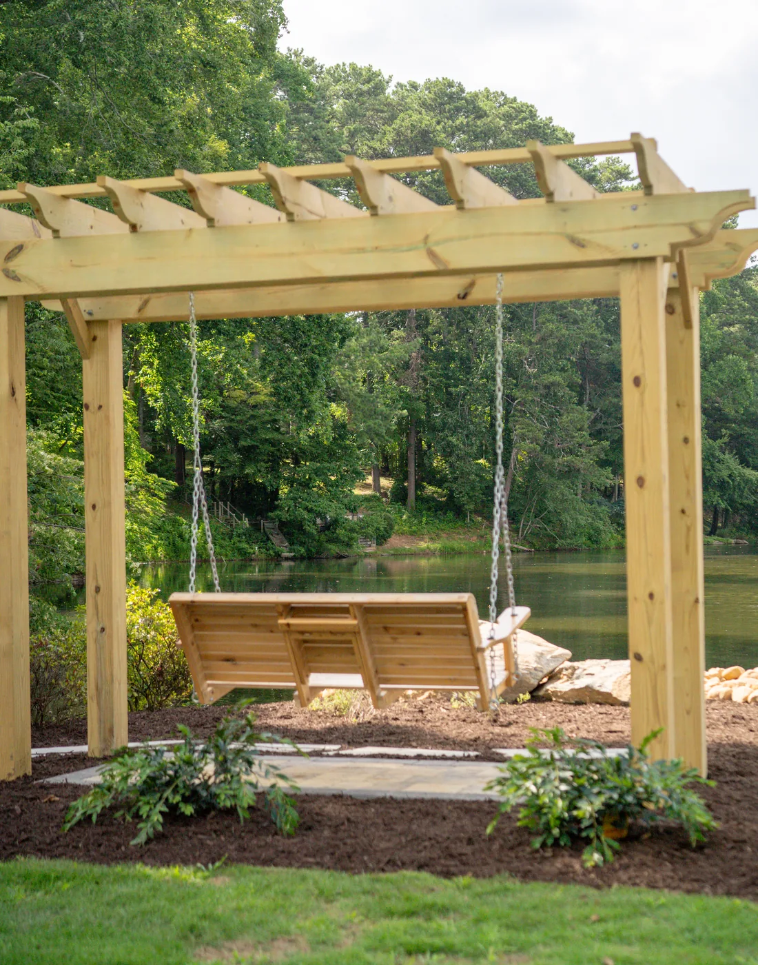 Cedar pergola with a porch swing over a fresh planting bed, built by KalKare