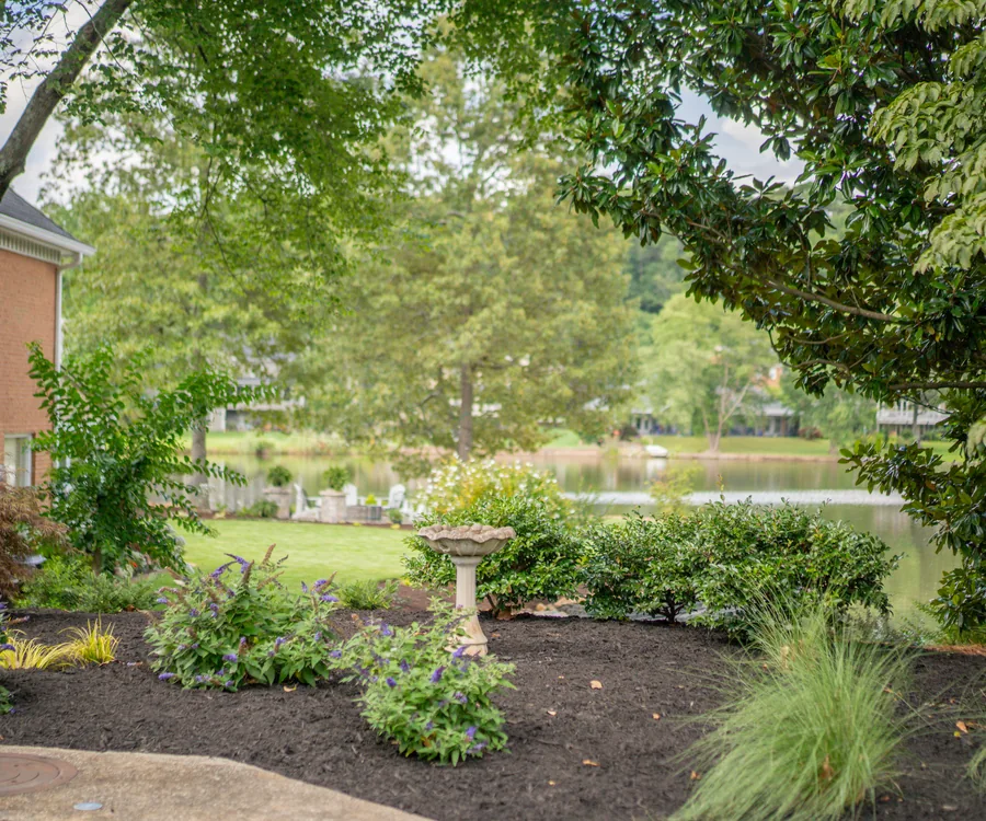 Designed garden bed with a birdbath and ornamental grasses beside a lake, by KalKare