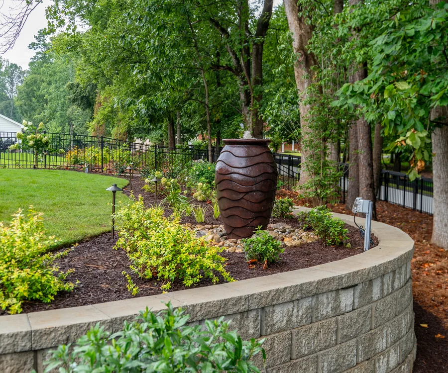 Stacked-stone retaining wall with a decorative urn and fresh plantings, built by KalKare