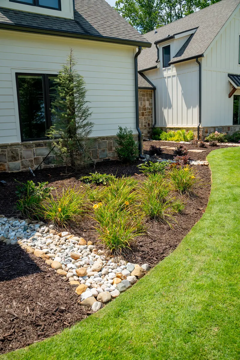 Foundation planting bed with a river rock drainage strip and ornamental grasses beside a modern home