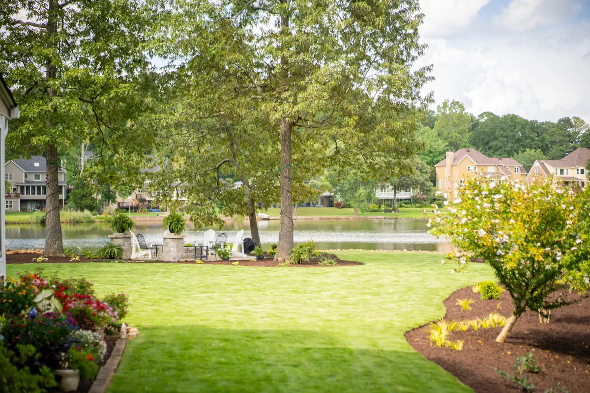 Finished lakefront backyard with a manicured lawn, mature shade trees and colorful planting beds