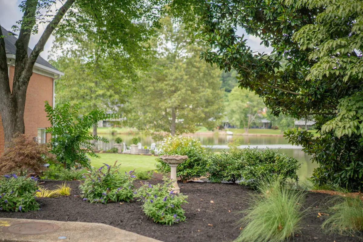 Lakeside planting bed with a stone birdbath, ornamental grasses and layered perennials