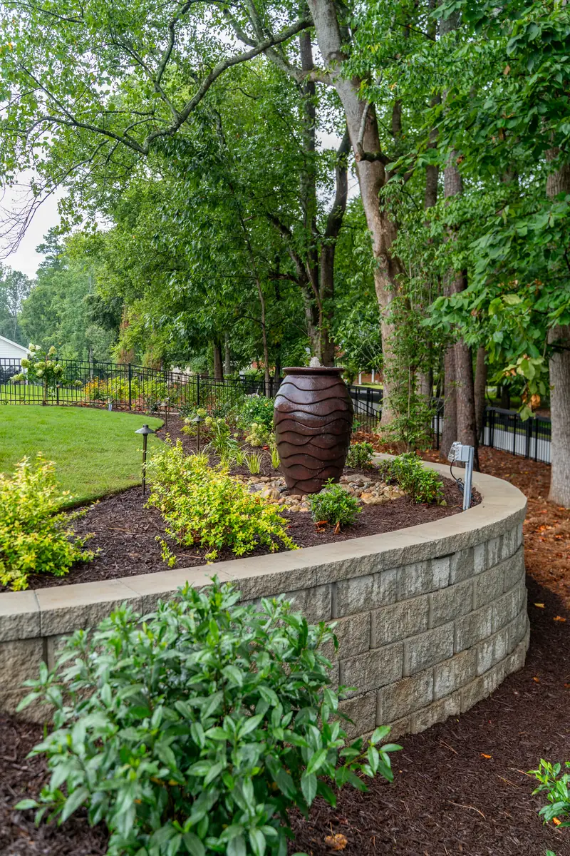 Curved stacked-stone retaining wall with a ceramic urn feature and layered shrub plantings