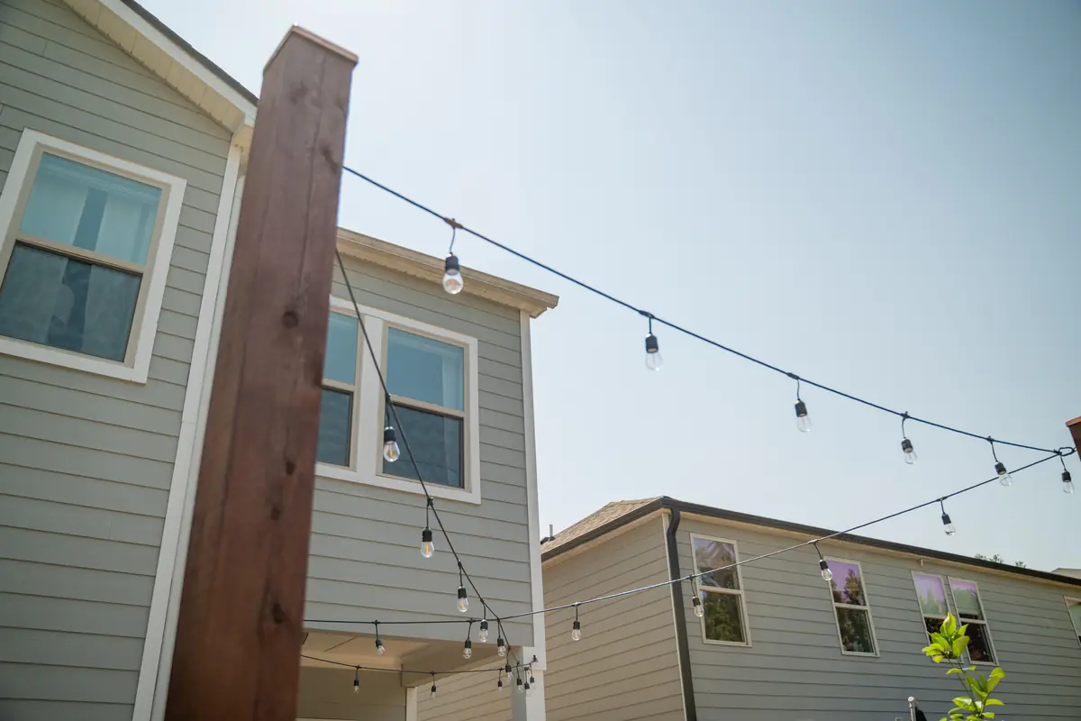 Cafe string lights strung from a cedar post between homes against a clear sky