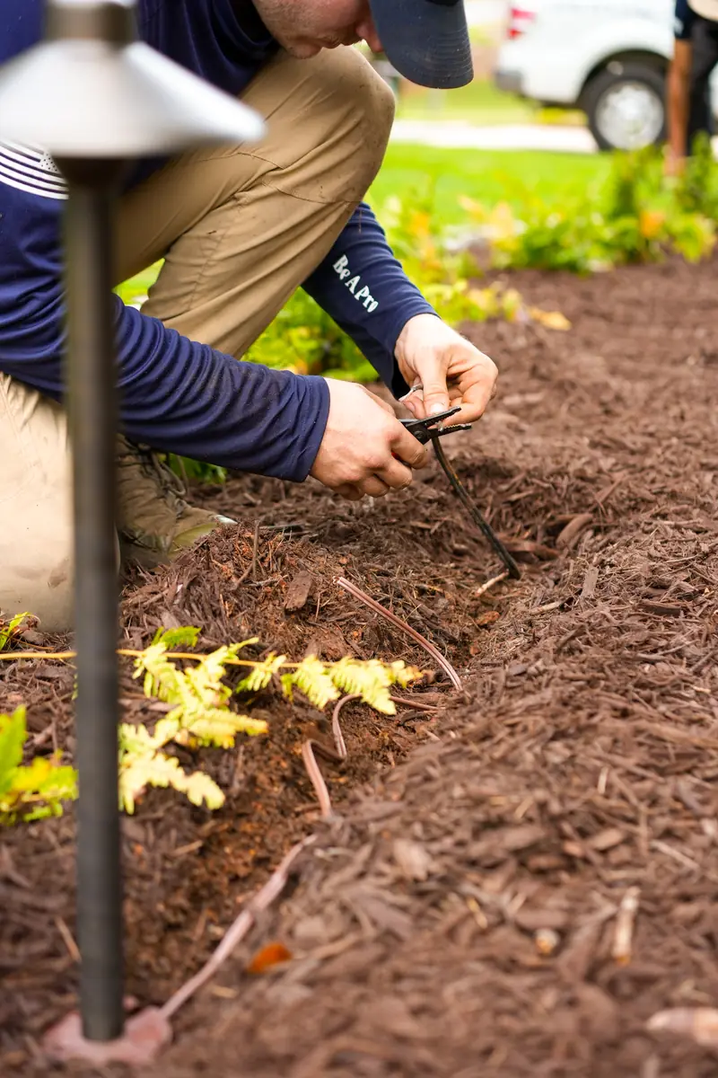KalKare technician wiring a low-voltage landscape light fixture in a mulched bed