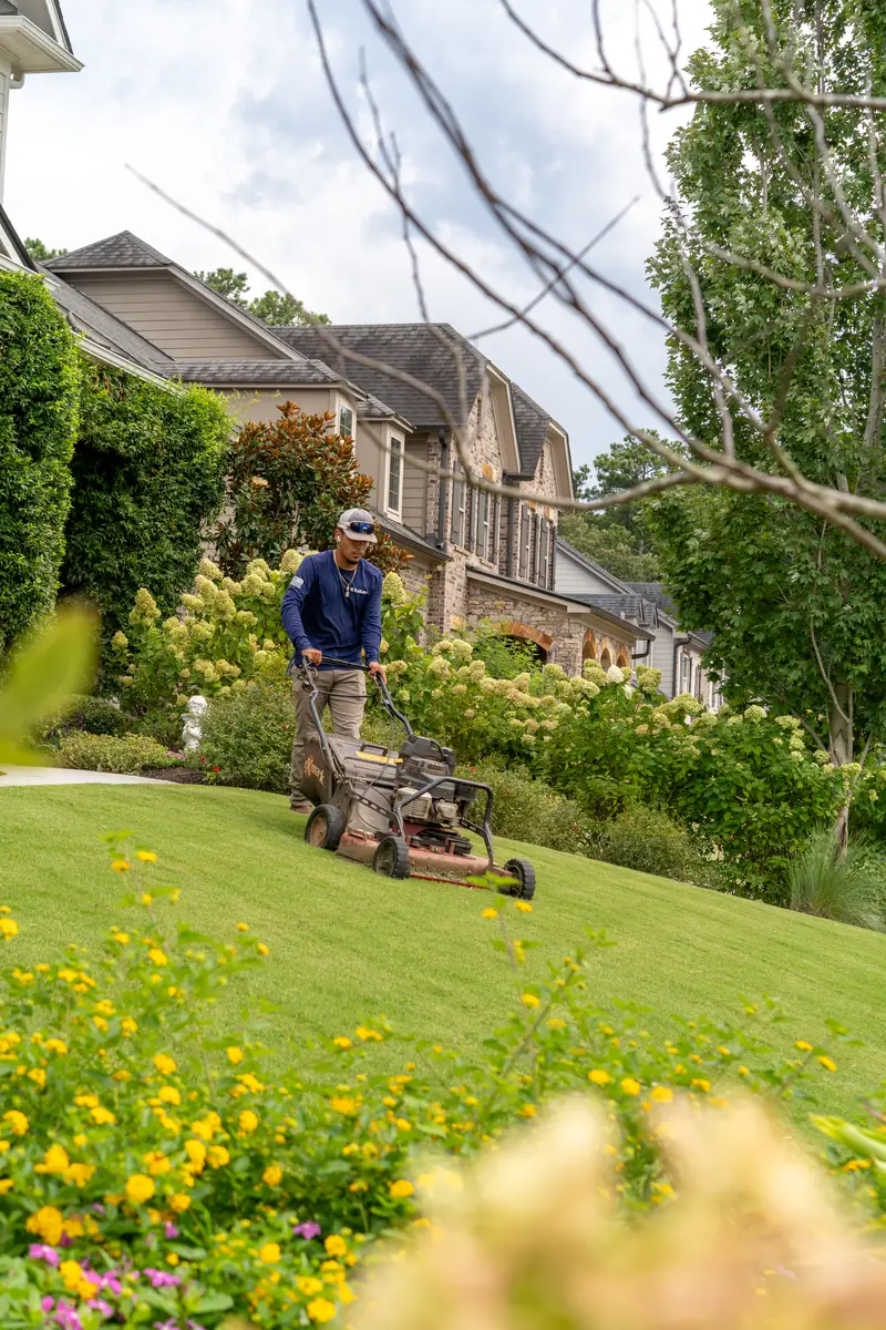 KalKare crew member mowing a sloped lawn in front of a stone estate home