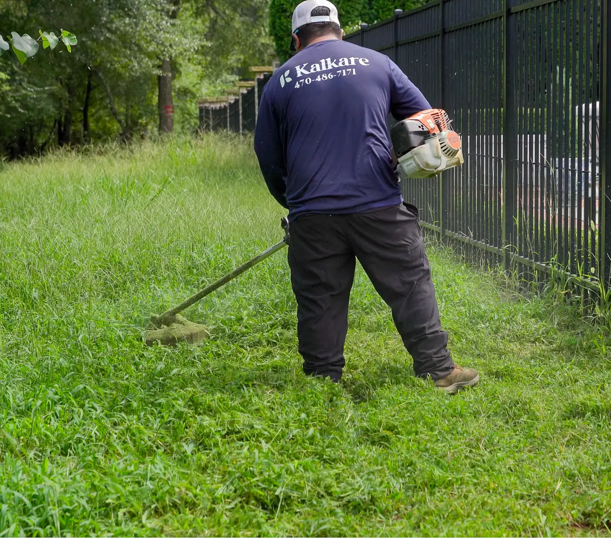 KalKare crew member trimming grass along a black iron fence during grounds maintenance