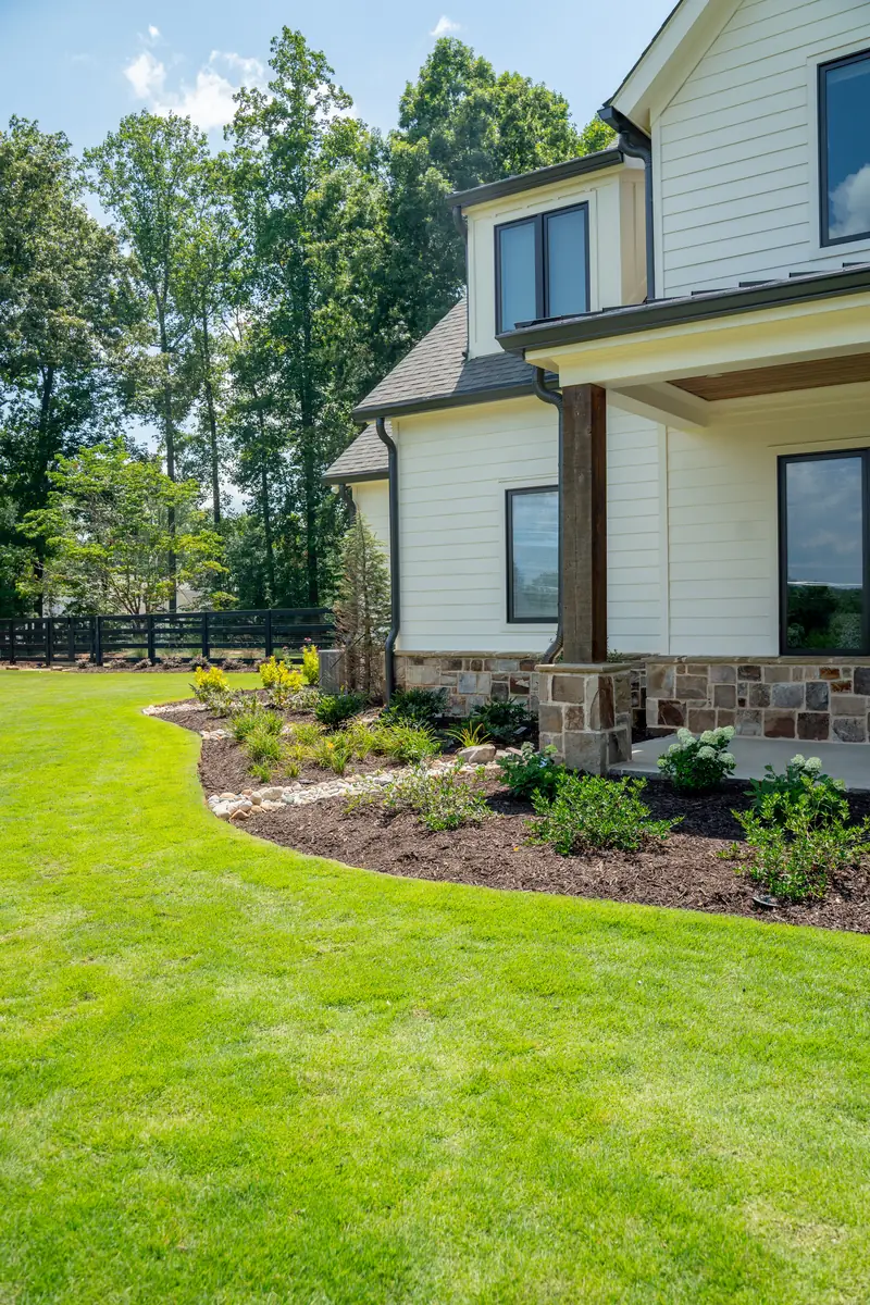 Manicured lawn and fresh mulched beds along a modern farmhouse with stone accents