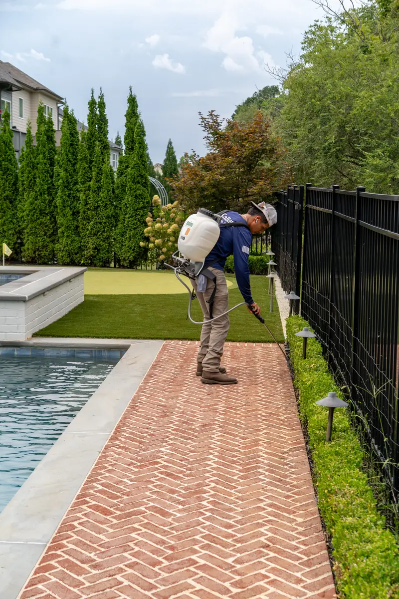 KalKare crew member clearing a brick paver walkway beside a pool during a seasonal cleanup