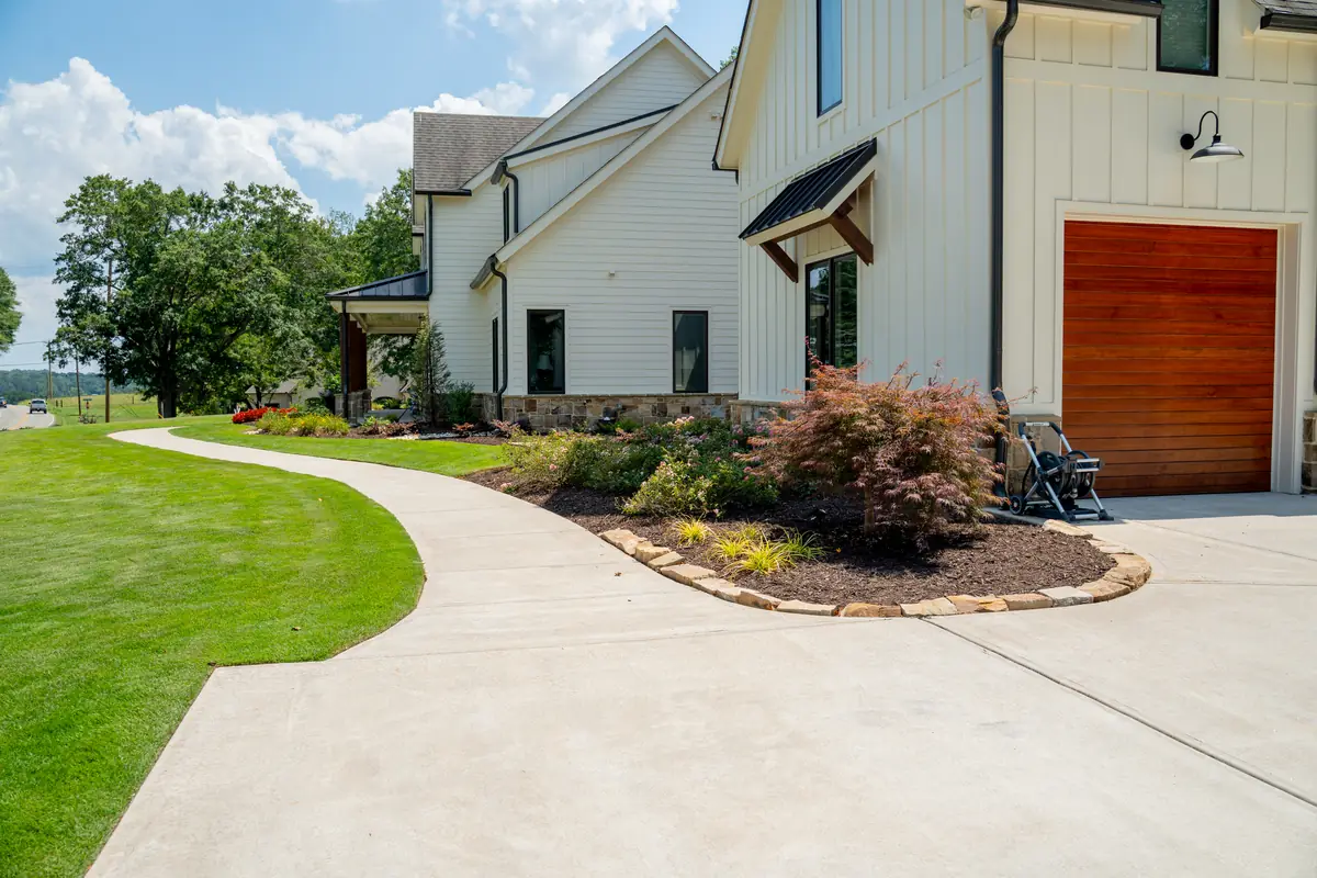 Clean, manicured lawn and freshly mulched beds with Japanese maples along a modern farmhouse driveway