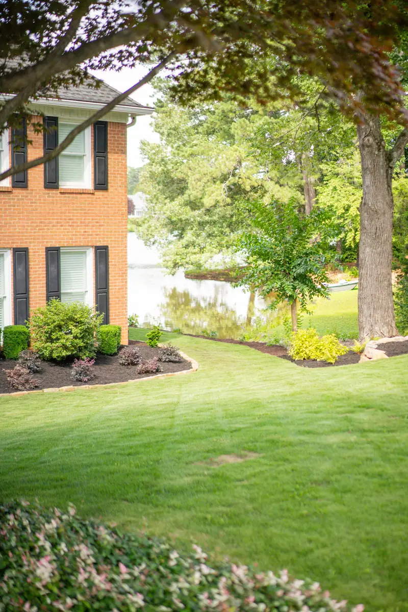 Healthy lakefront sod lawn beside a brick home with mulched foundation beds