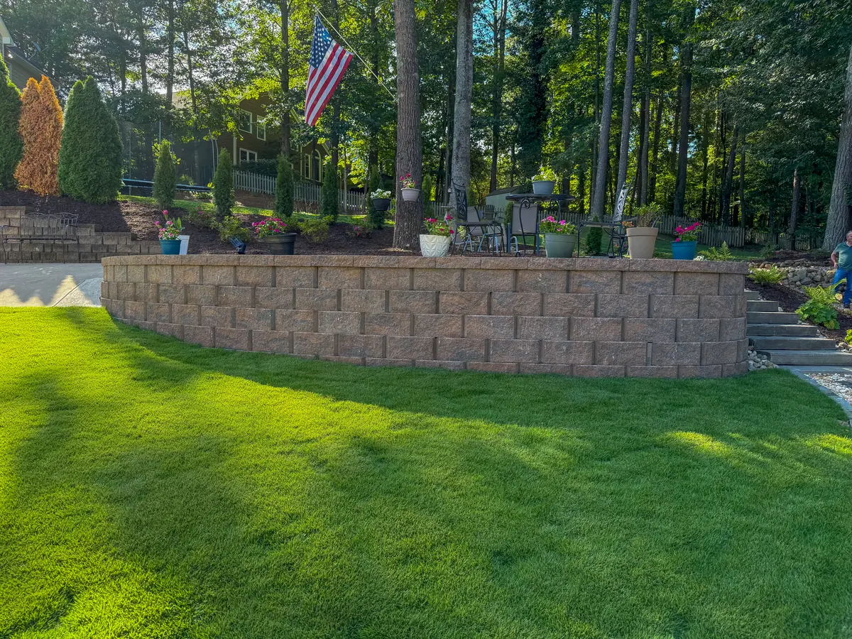 Lush sod lawn beside a stacked block retaining wall with potted flowers
