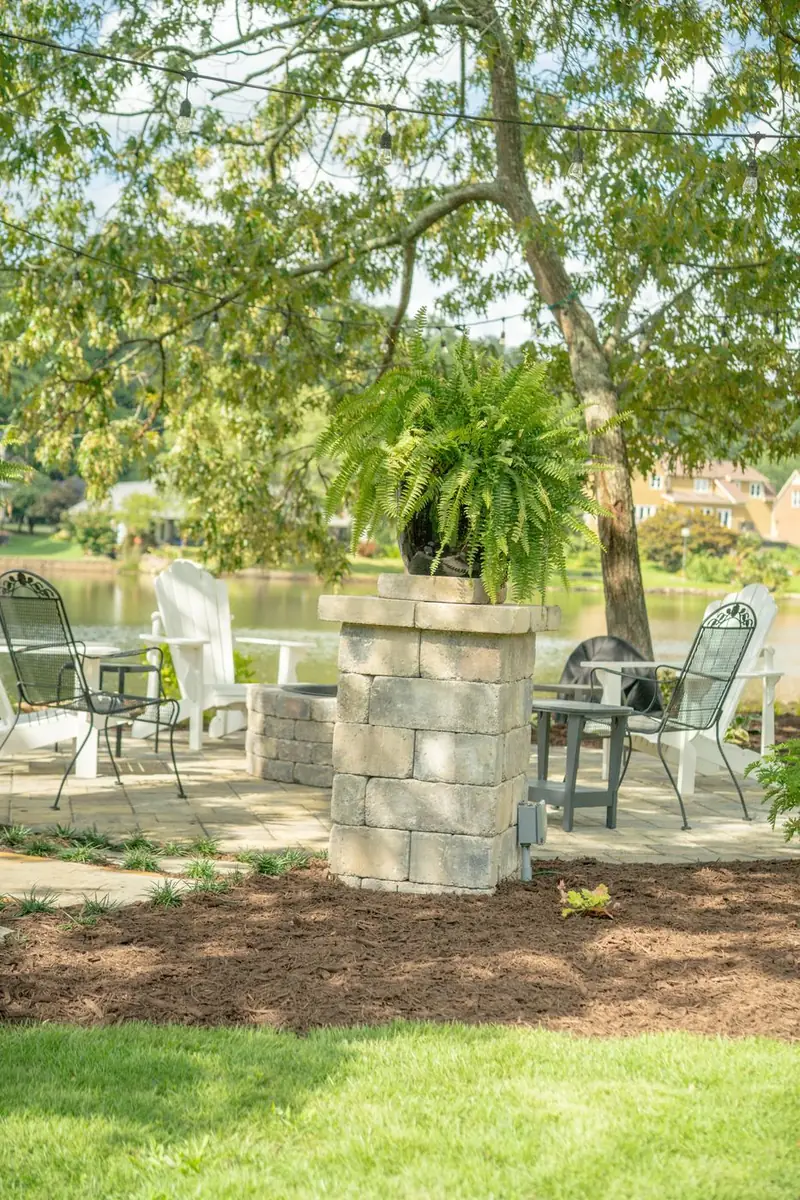 Stone pillars with ferns framing a lakeside patio seating area.